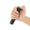 Hand holding a black tactical flashlight pressing the tail cap switch on a white background