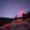 Hiker wearing a red headlamp walking on rocky terrain at night under a purple twilight sky