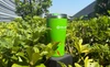 Olight green stainless steel travel tumbler with red splash pattern placed outdoors in lush green bushes