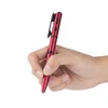 Hand holding a metallic red multi-function tactical pen with writing tip, pocket clip, and buttons, isolated on white background