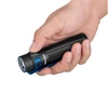 Hand holding an Olight Warrior Mini 3 flashlight with a blue clip and switch, showing its textured grip and lens.