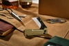 Compact folding utility knife with gold handle and ceramic blade on canvas work mat near EDC tools