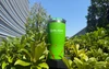 Olight lime green insulated travel tumbler with red splatter pattern on outdoor display surrounded by lush green bushes