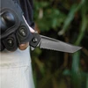 Person in tactical glove holding a black SENTRY L2 folding knife with a partially serrated tanto blade.