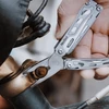 Hand holding NexTool multi-tool pliers to tighten a rusty bolt on a bicycle frame