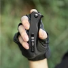Tactical folding knife with carbon fiber handle held by a gloved hand outdoors.