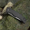 Black carbon fiber folding knife, closed, on mossy rock. Perfect for EDC and outdoor use.