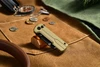 Closed sand-colored EDC pocket knife on a brown canvas mat with coins, compass, and outdoor gear.