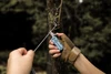 Person in tactical gloves using a blue pocket multitool to cut wire outdoors