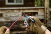 Gloved hand using NexTool multitool pliers to cut a red wire outdoors