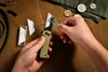 Hands changing white ceramic utility blade on folding pocket knife with tool over brown canvas workspace