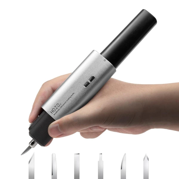 Hand holding HOZO NeoBlade ultrasonic cutting knife with interchangeable blades below for precise crafting.