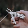 Hand holding a NexTool multi-tool plier cutting metal wire outdoors