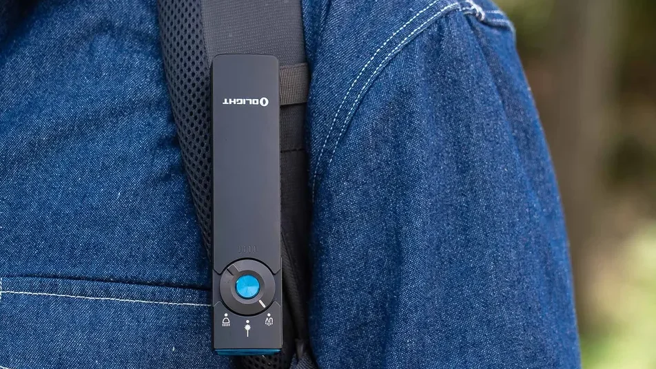 Olight clip light on backpack strap, person in denim shirt, outdoor hiking gear.