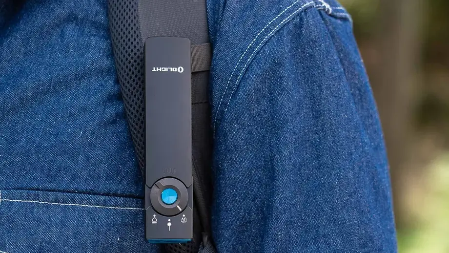 Olight clip light on backpack strap, person in denim shirt, outdoor hiking gear.