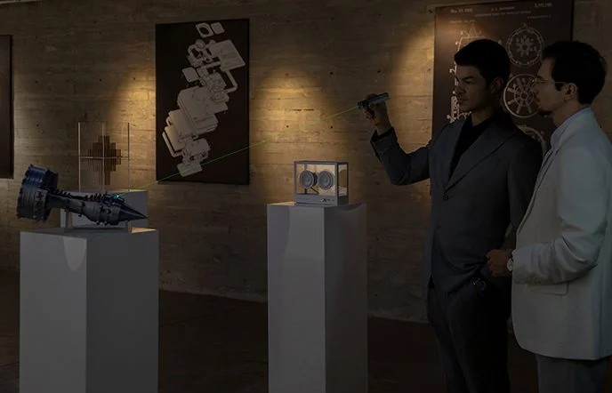 Two men examining tech exhibits with a laser pointer: a jet engine model, transparent speaker, and wall schematics.