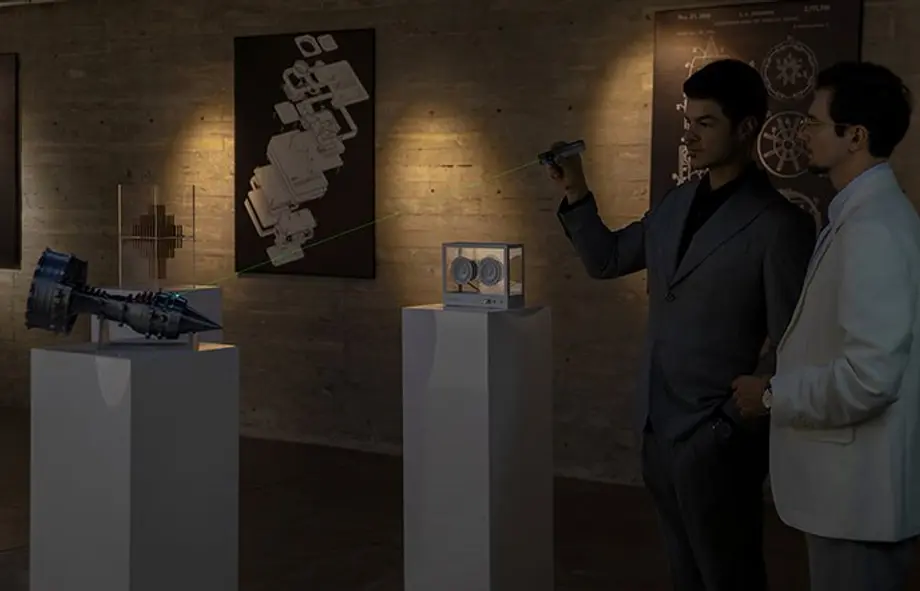 Two men examining tech exhibits with a laser pointer: a jet engine model, transparent speaker, and wall schematics.