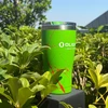 Olight lime green insulated travel tumbler with red splatter pattern standing among lush garden plants outdoors