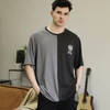 Young man wearing a two-tone black and grey graphic tee, black pants, hands in pockets.