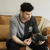 Young man in black and gray color block t-shirt reading a magazine on a brown sofa.