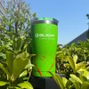Green Olight travel tumbler with red splatter pattern outdoors surrounded by green leaves under a blue sky