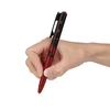 Hand holding a red and black voice recorder pen with a power button and clip isolated on white background