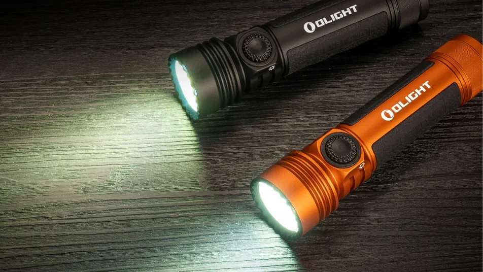 Two Olight flashlights, black and orange, shining bright on dark wood.