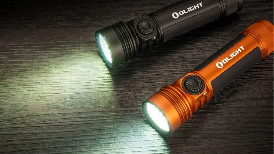 Two Olight flashlights, black and orange, shining bright on dark wood.