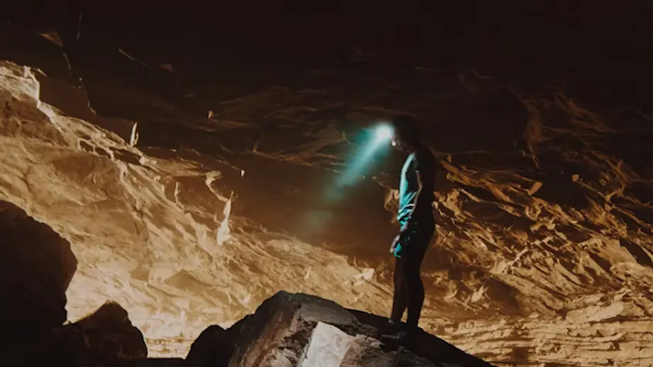 Person with headlamp exploring dark cave, light illuminates textured rock formations.