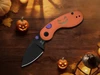 Halloween themed folding pocket knife with orange pumpkin handle and black blade on wooden background with mini jack-o-lanterns