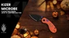 Kizer Microbe pocket knife with orange Halloween Jack-O-Lantern handle on a wooden background with pumpkins