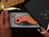 Kizer Halloween pocket knife with orange pumpkin handle and purple thumb studs inside a black gift box