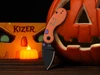 Kizer Halloween themed pocket knife with orange handle and black blade next to carved pumpkin lantern