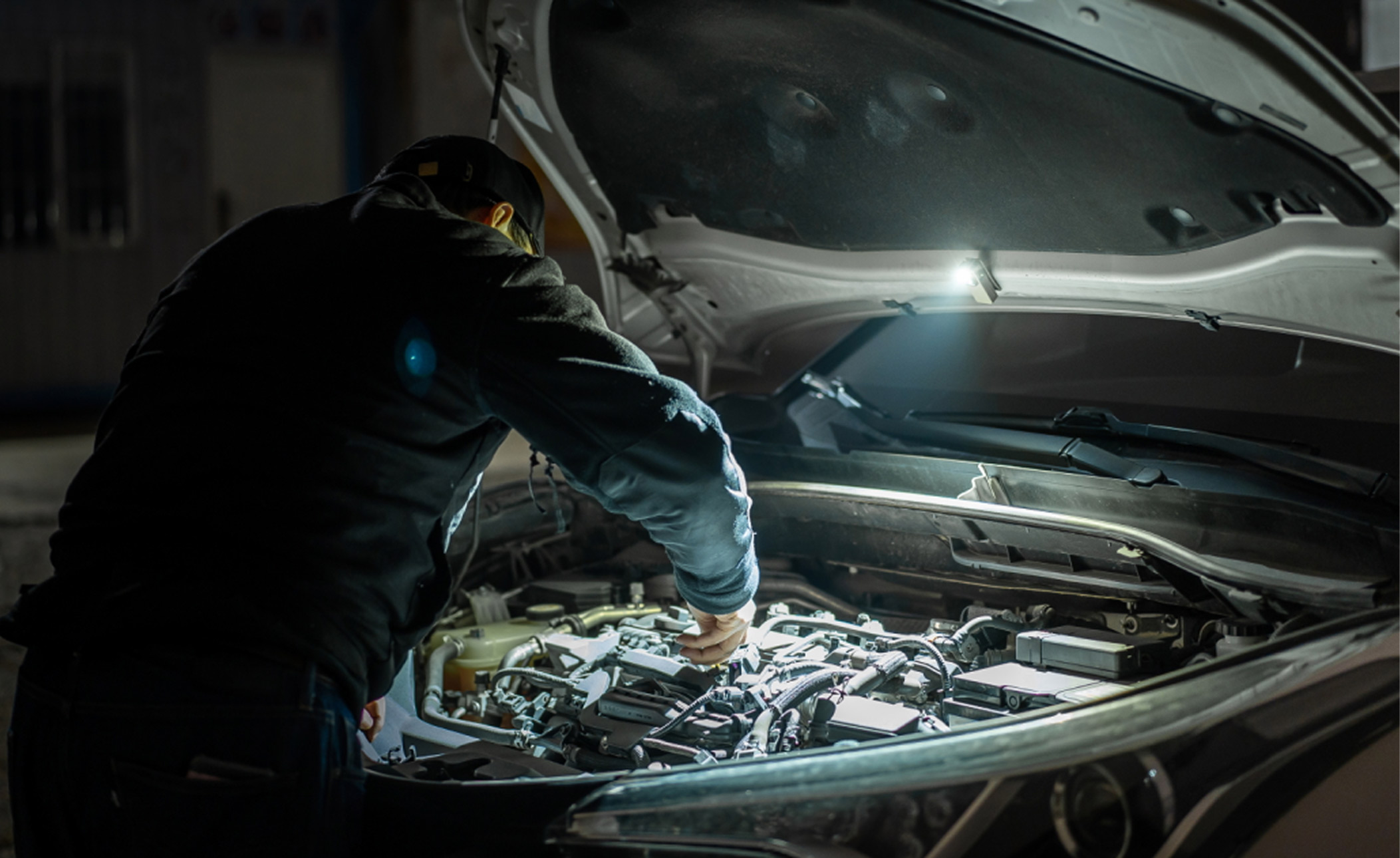 A man repairing a car engine at night with Olight illumination, text: 'When things break, he's there to fix them.'